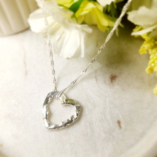 Silver heart-shaped necklace on a white surface with flowers in the background